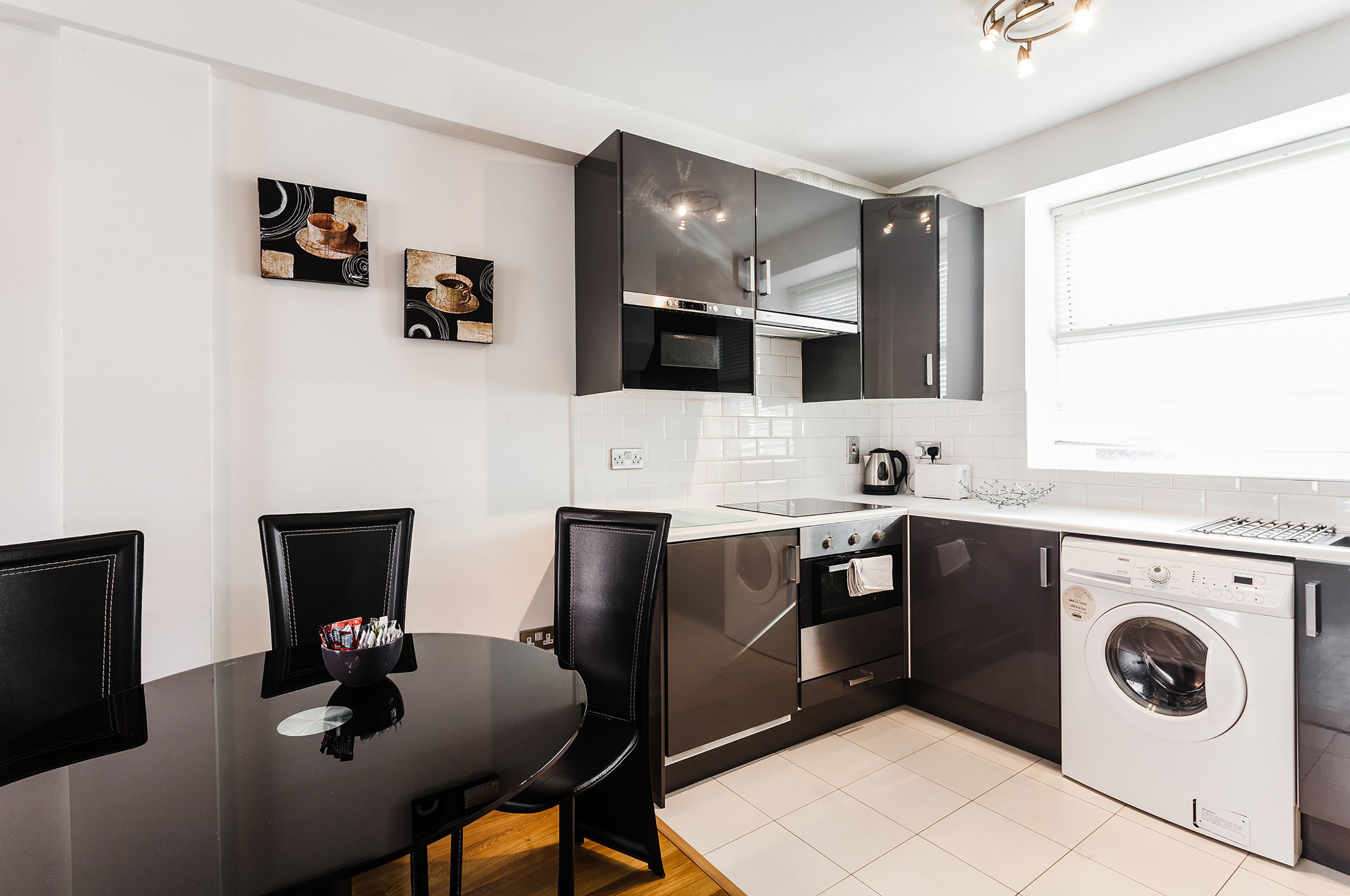 A modern kitchen with black cabinets, a stainless steel oven, a microwave, and a built-in washing machine.