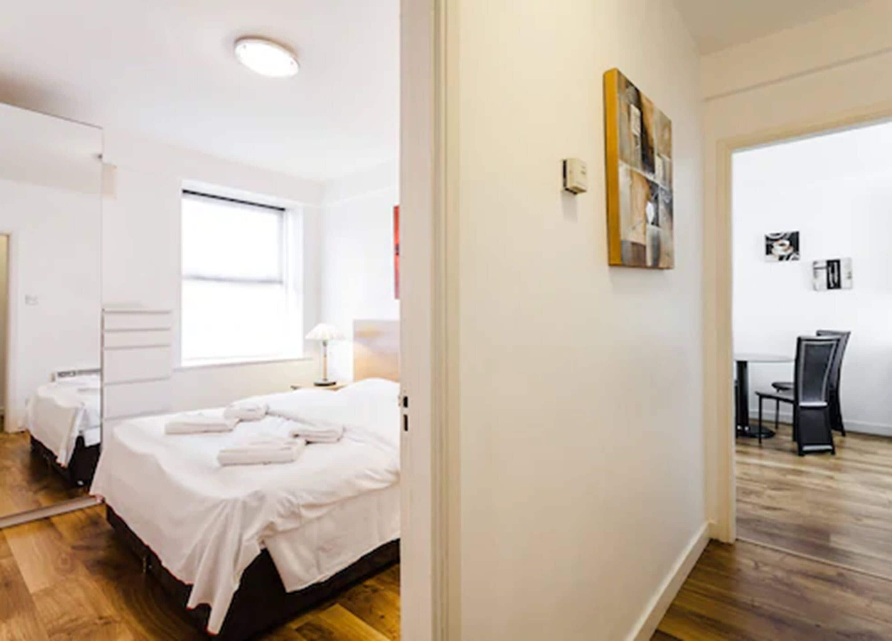 A hotel room with a bed, a bedside table, a lamp, and a window.