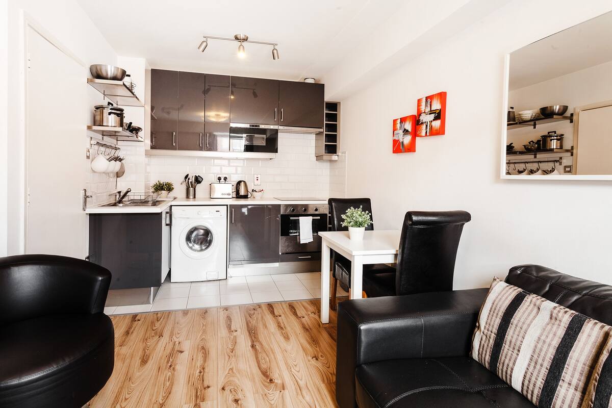A compact kitchen with modern appliances, a dining area with a table and chairs, and a living area with a sofa and a coffee table.