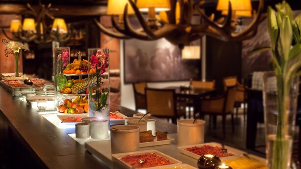 Ein reichhaltiges Buffet mit verschiedenen Speisen und Getränken, darunter Früchte, Desserts und Erfrischungen, auf einer langen Tafel mit angenehmer Beleuchtung.