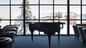 Ein Klavier in einem Raum mit großen Fenstern, einem Kerzenleuchter und Reihen von Stühlen.