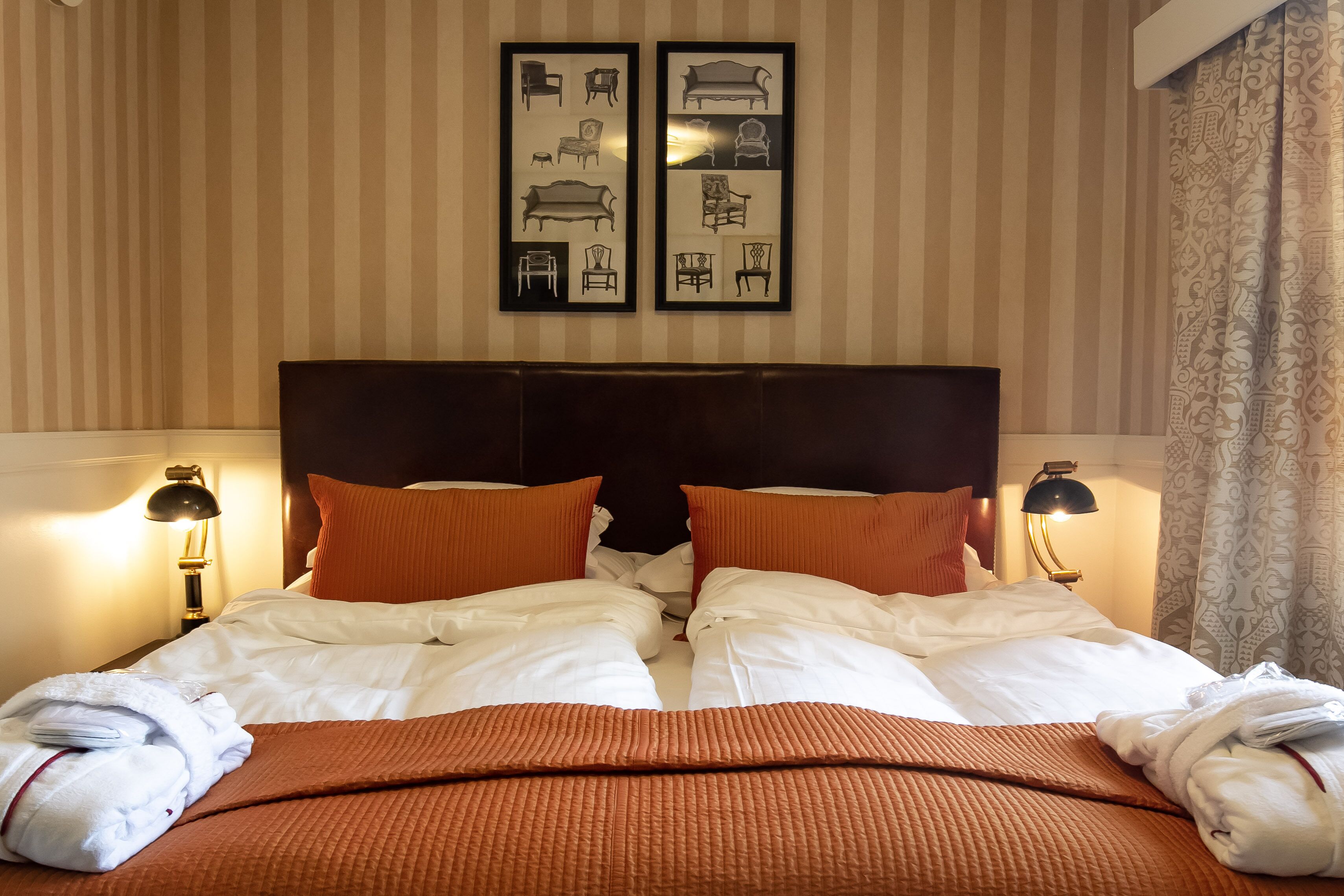 A hotel room with a large bed, two bedside lamps, striped wallpaper, and a headboard.