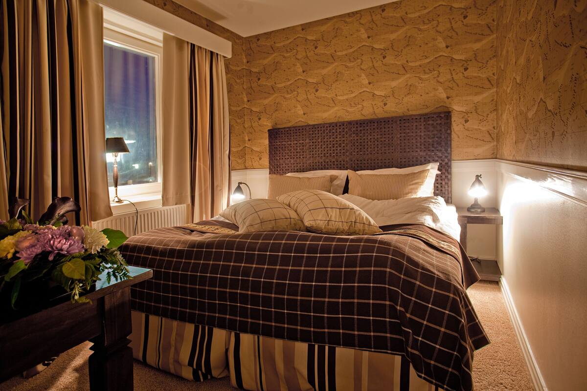 Een hotelkamer met een groot bed, een nachtkastje, een lamp en een raam met gordijnen.