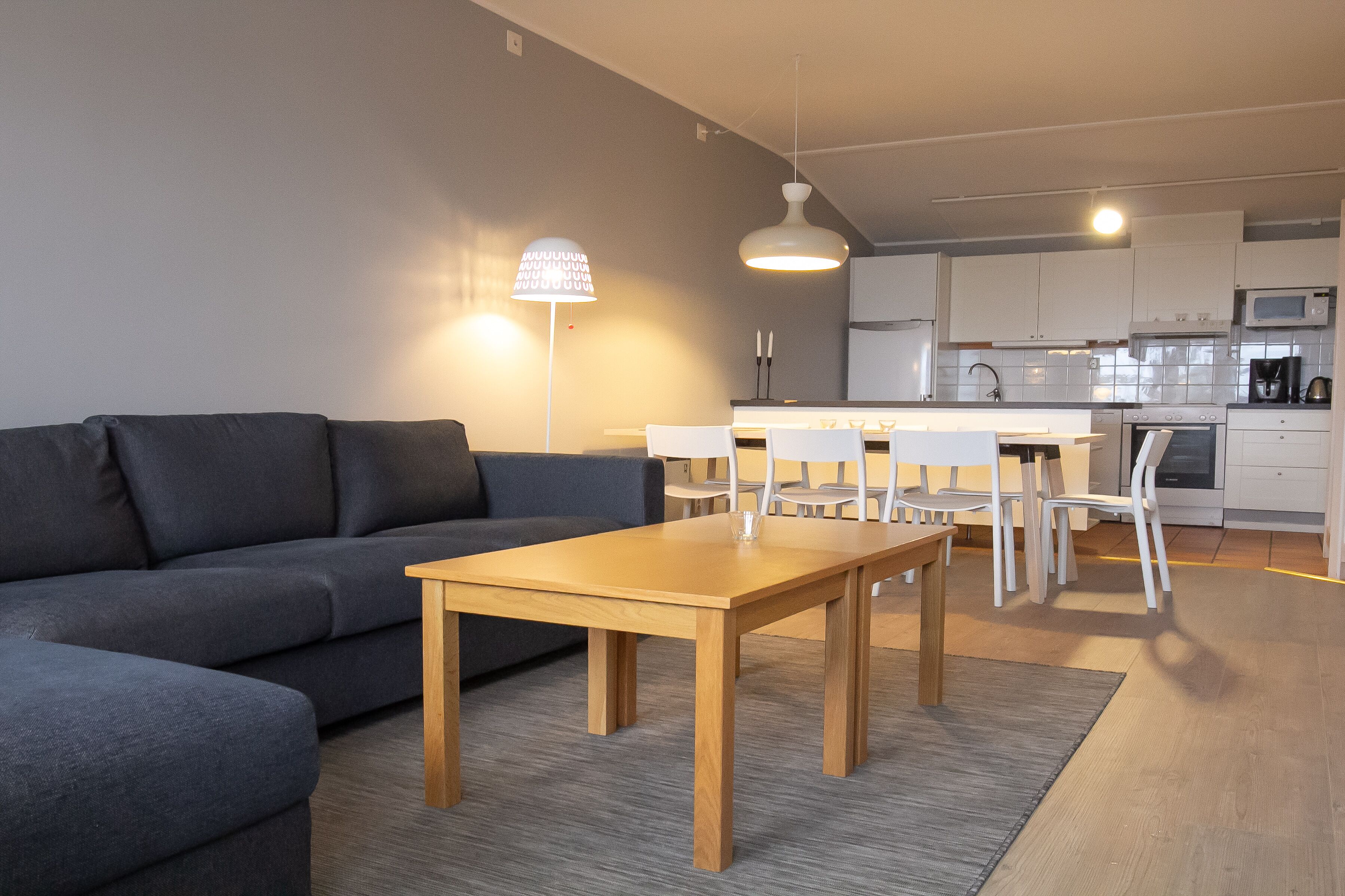 A modern living room with a sofa, a wooden table, and a dining area with chairs.