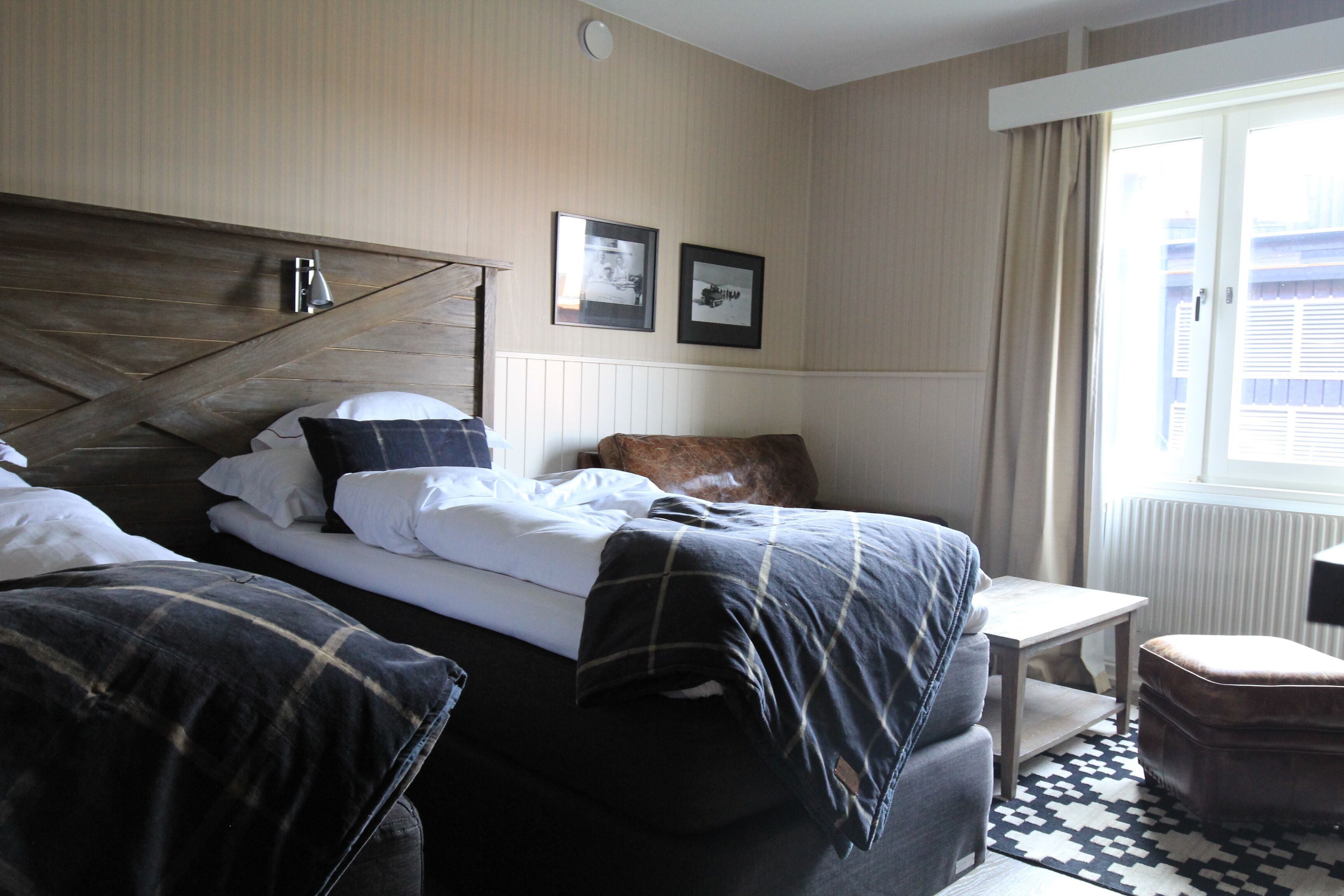 Habitación de hotel con cama, una mesita, una silla y un ventanal con cortinas.