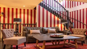 A living room with a leather sofa, two armchairs, a coffee table, and a staircase with striped walls.