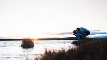 A sunset over a calm body of water with two people crouching near the edge.