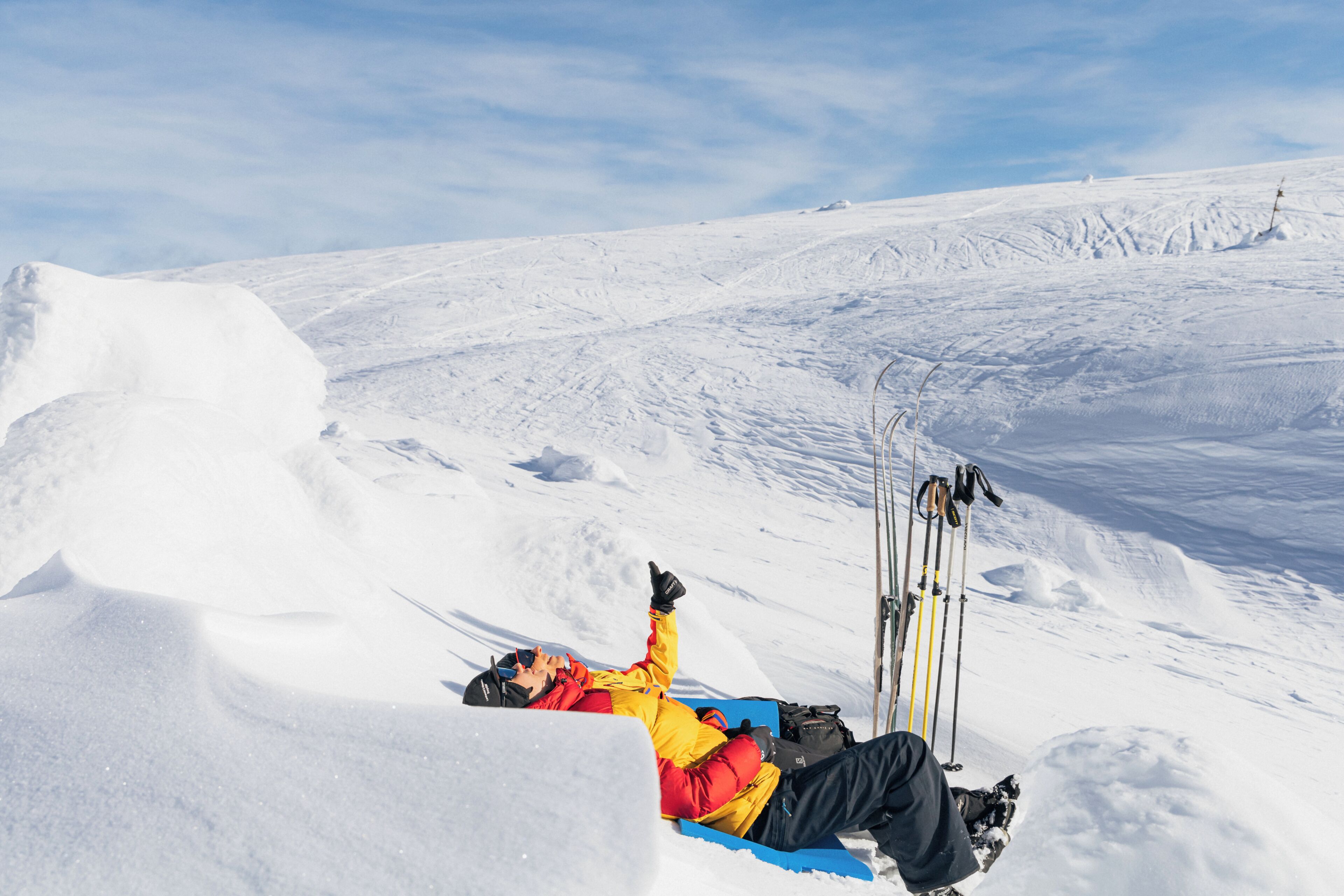 A person lying on a snowy slope with skis and poles nearby.