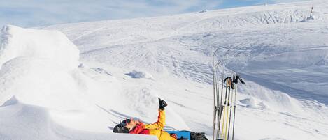 A person lying on a snowy slope with skis and poles nearby.