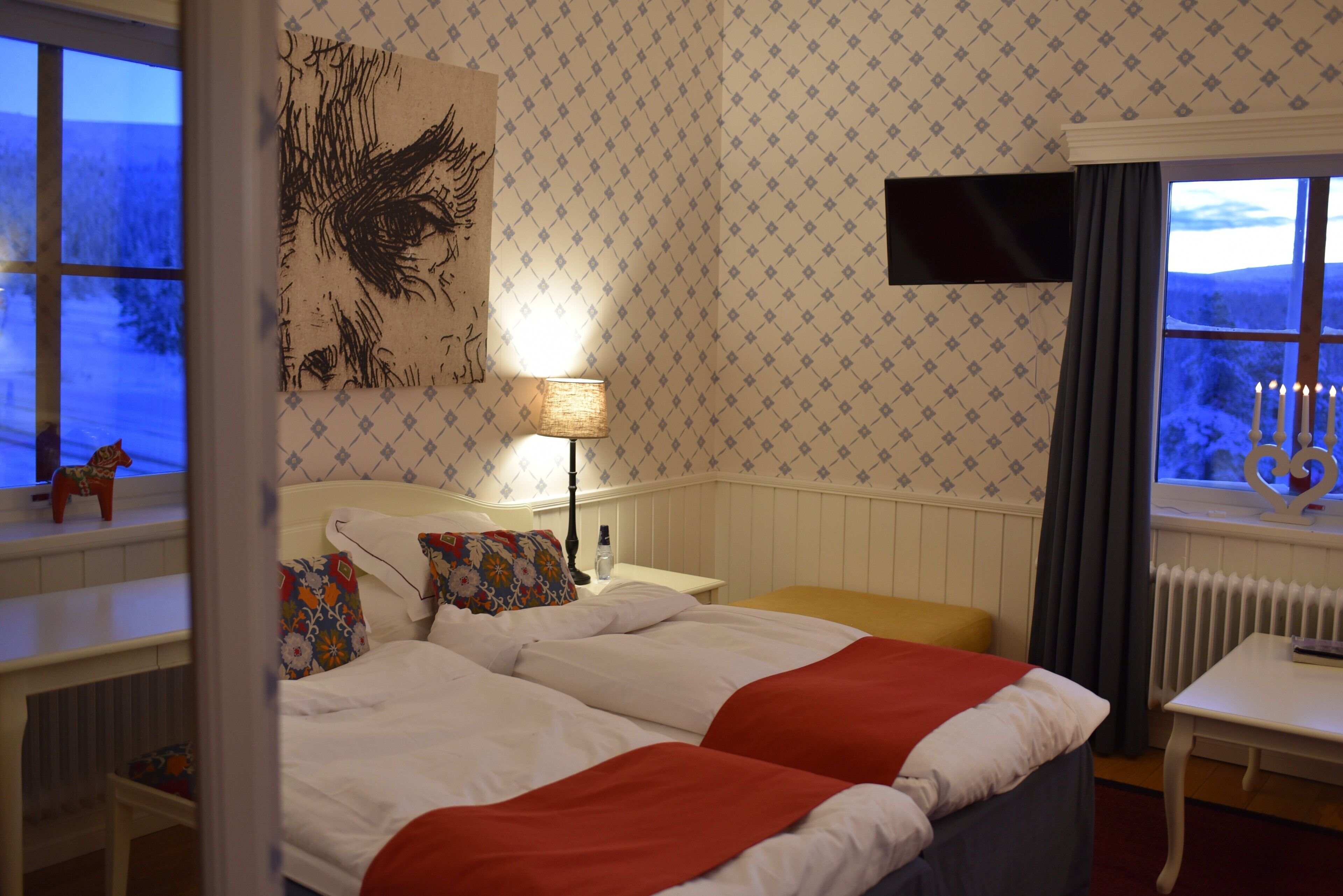 Habitación de hotel con dos camas, un televisor montado en la pared, una ventana con vistas al exterior y una lámpara en una mesita de noche.