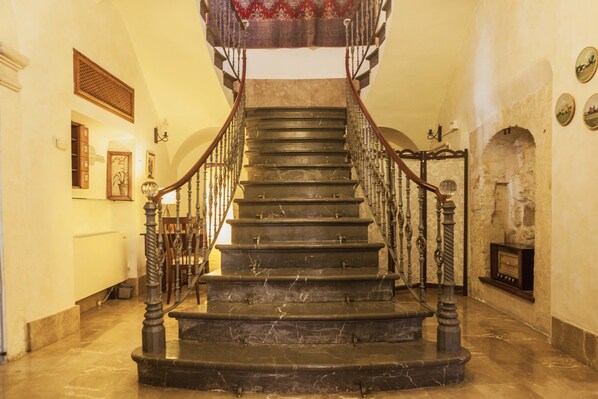 A grand staircase with marble steps and wooden railings, leading to a landing with a red carpet.
