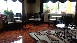 A dining area with wooden chairs and tables, a patterned rug, and potted plants. - Scottish Inn & Suites (Houston)