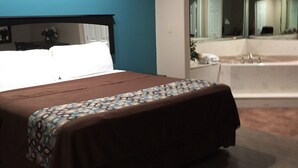 A bedroom with a bed, a bathroom with a bathtub, and a large mirror. - Scottish Inn & Suites (Houston)