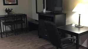 A hotel room with a desk, chair, TV, lamp, and a framed picture on the wall. - Scottish Inn & Suites (Houston)