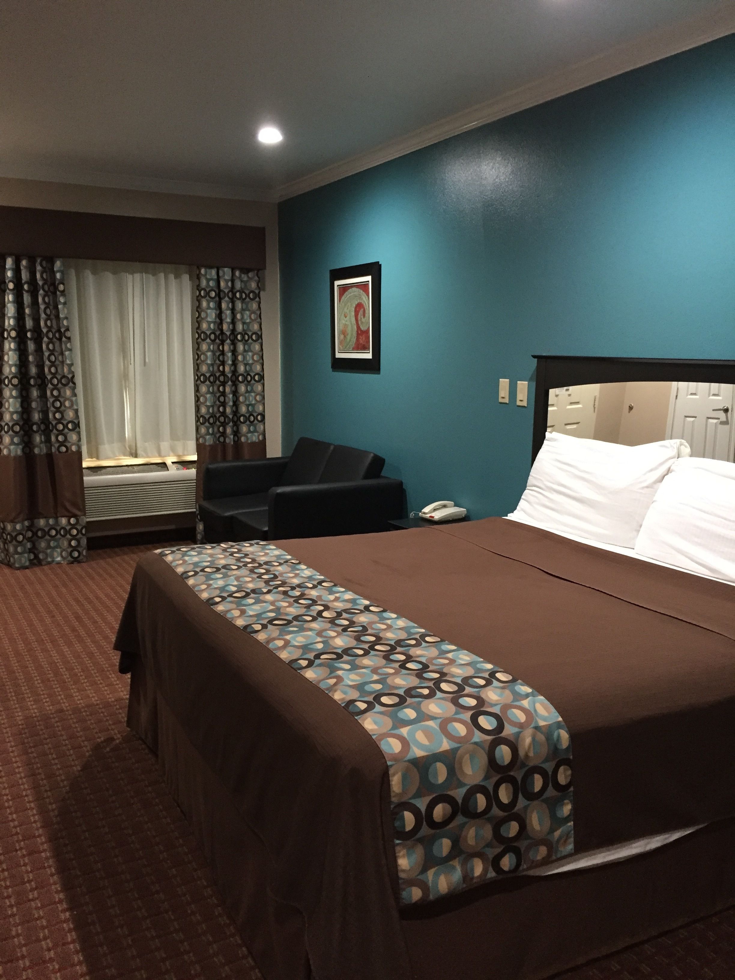 A hotel room with a bed, a desk, a chair, and a window with curtains.