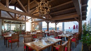 Un restaurante con mesas y sillas de madera, un techo alto con vigas a la vista, y vista al mar.