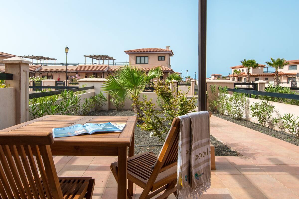 Une table et des chaises en bois, placées sous une pergola, offrent une vue dégagée sur un quartier résidentiel.