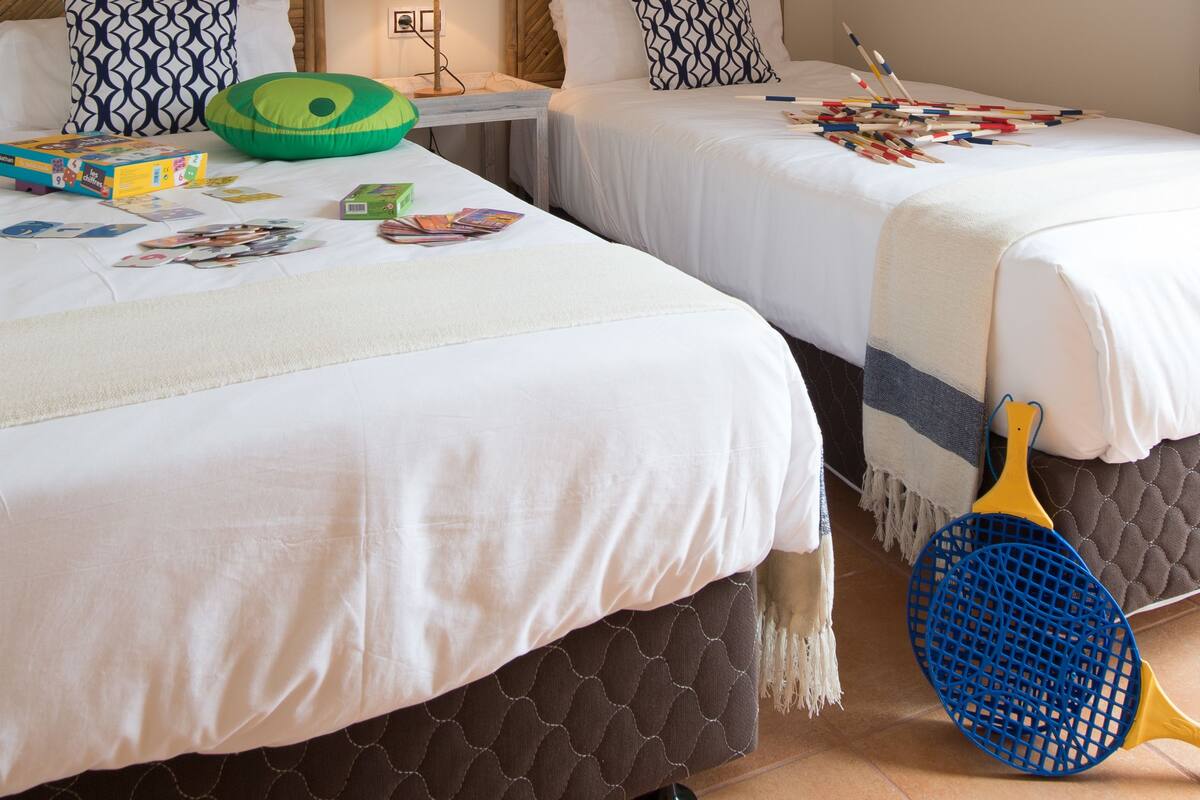 Une chambre d’hôtel avec deux lits, une lampe et une pagaie bleue et jaune posée sur le sol.