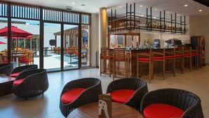 Un restaurante con sillas de mimbre, una zona de bar con estantes llenos de vasos, y vistas amplias a través de grandes ventanales.
