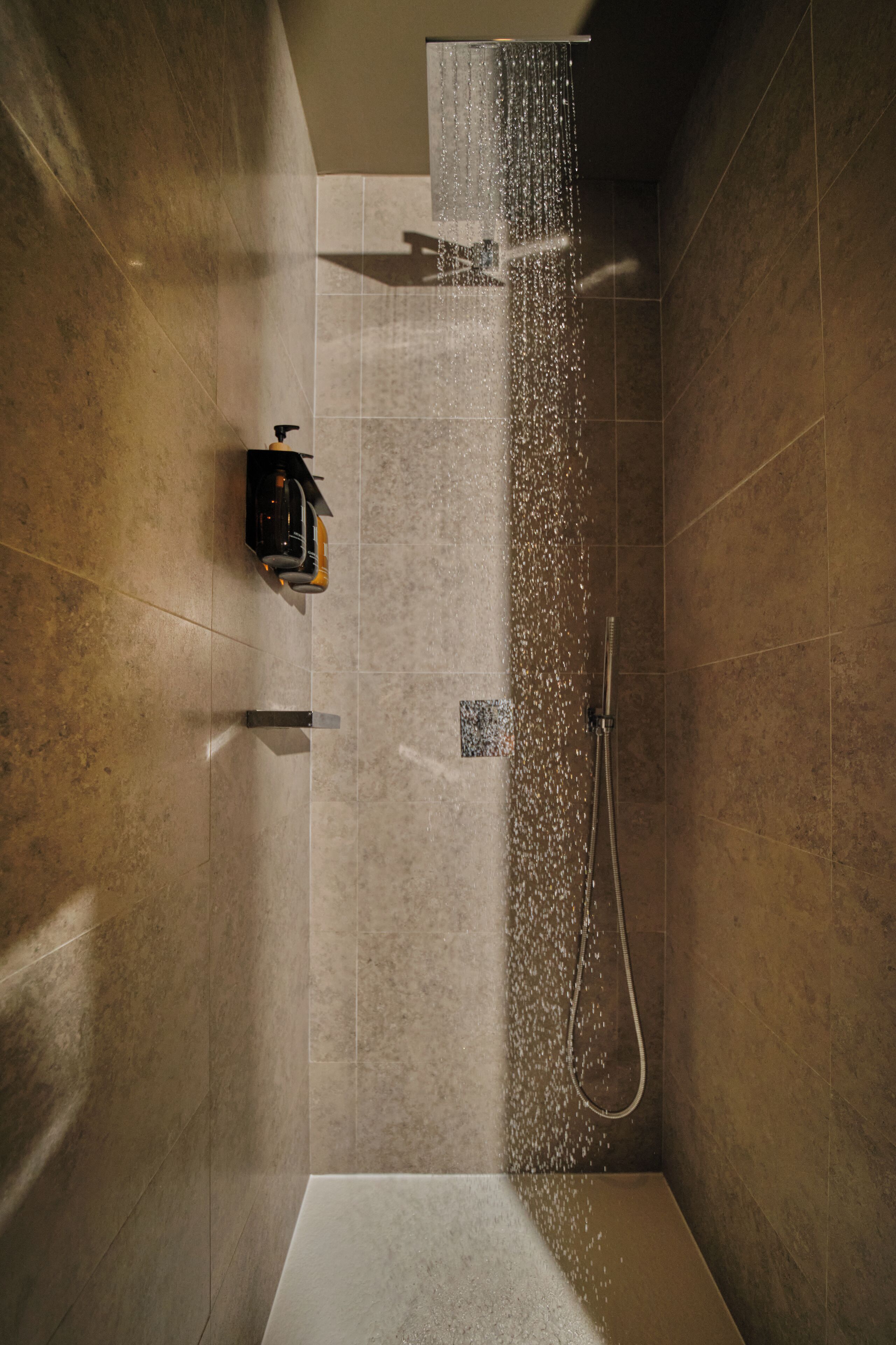 A shower area with a handheld showerhead and a wall-mounted faucet.