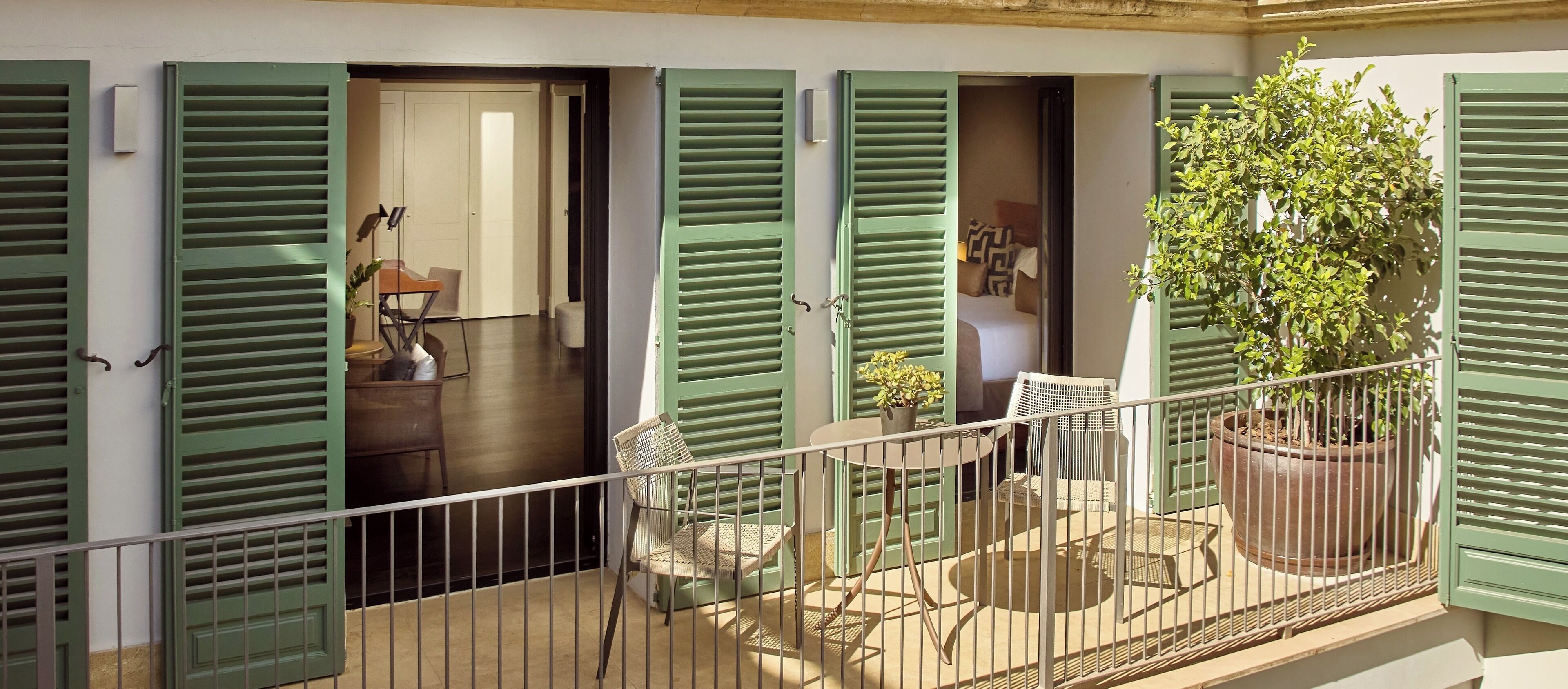 A balcony with green shutters, a potted plant, and a small table with chairs.