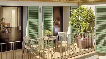 A balcony with green shutters, a potted plant, and a small table with chairs.