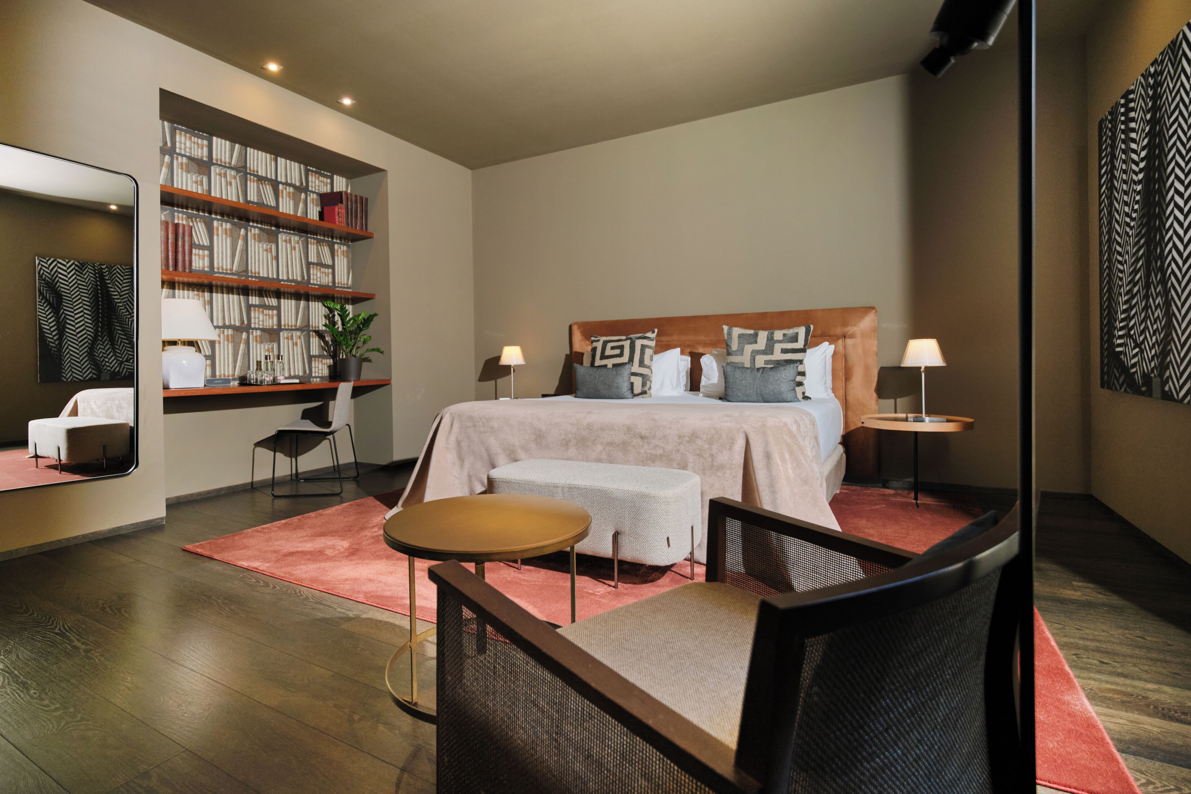 Une chambre d’hôtel moderne avec un grand lit, un coin salon avec une petite table, une bibliothèque et un miroir.