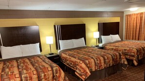 Ein Hotelzimmer mit drei Betten, jeweils mit einem gemusterten Überwurf, einem Nachttisch mit Lampe und einem Kopfteil mit Leuchte.