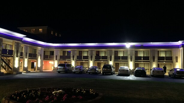 Ein Hotel mit einer Reihe geparkter Autos vor der Fassade, einem angelegten Gartenbereich und einem Gebäude mit flachem Dach und mehreren Balkonen.