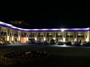 Un hotel con una fila de coches aparcados en la entrada, un jardín ajardinado y un edificio de techo plano con varios balcones.