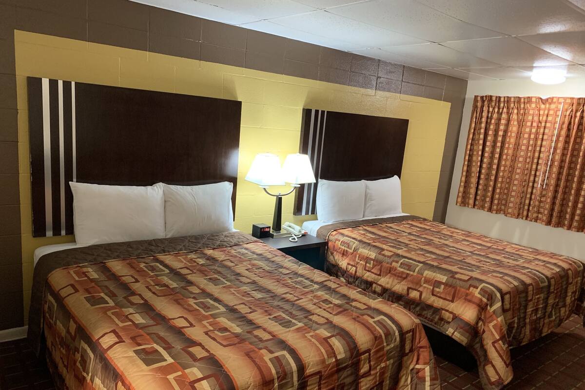 A hotel room with two beds, each with patterned bedding, a nightstand with a lamp, and a clock.
