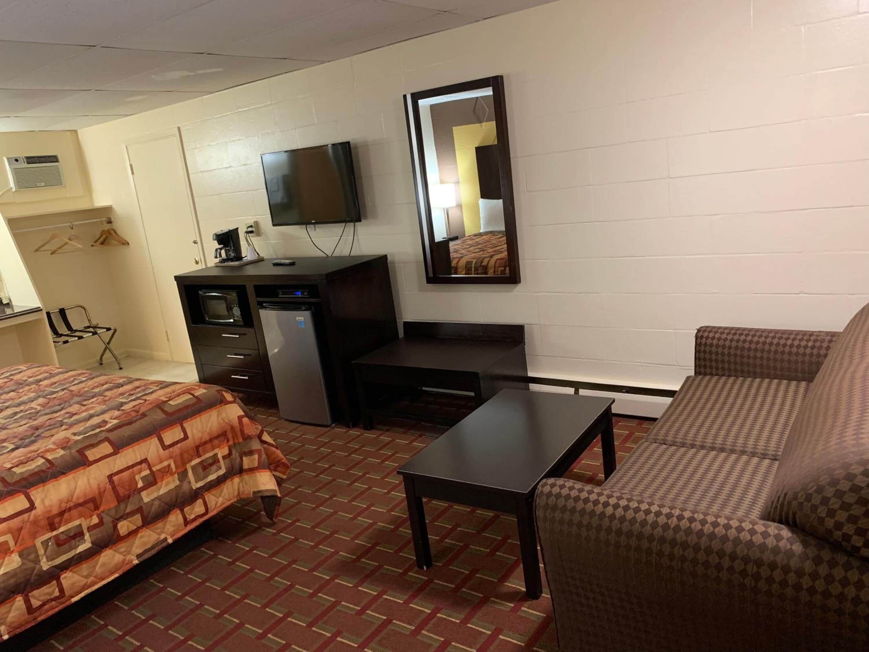 A hotel room with a bed, a desk, a chair, a small table, a TV, and a mirror.