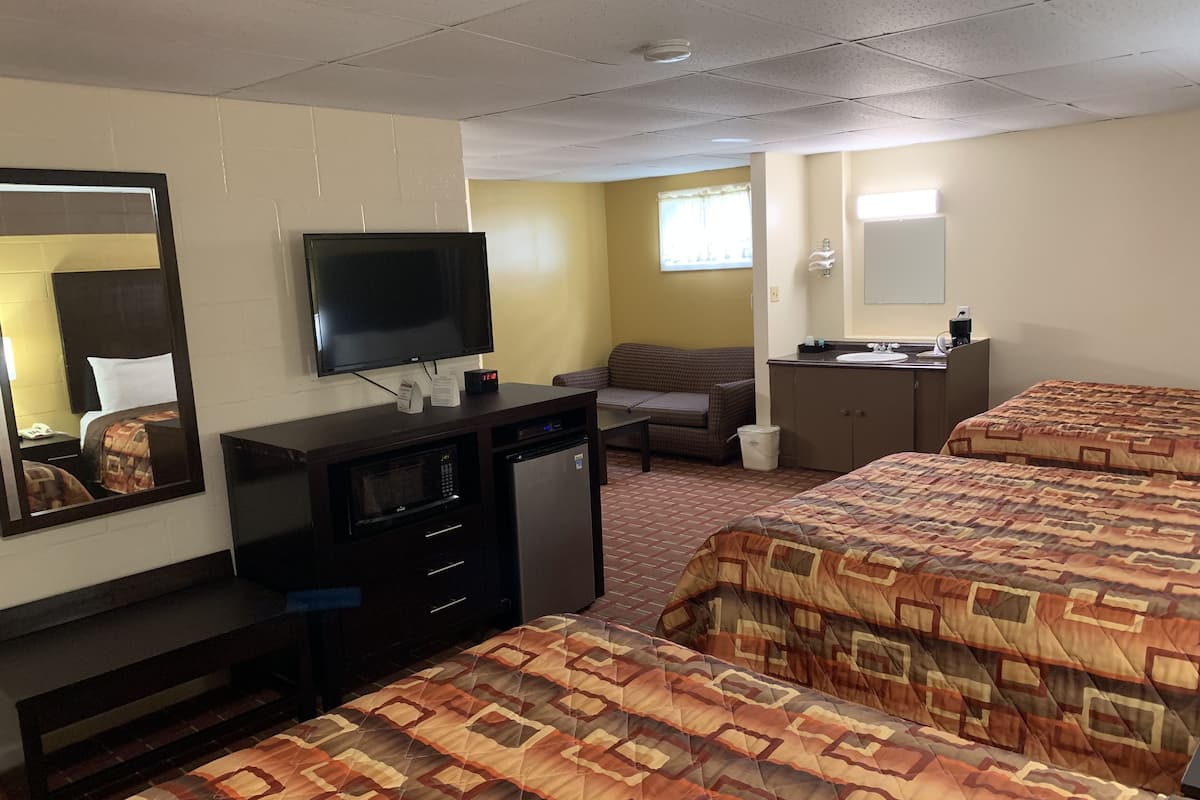 A hotel room with two beds, a TV, a desk with a microwave, a small table, a sofa, a bathroom with a sink and mirror, and a window with curtains.
