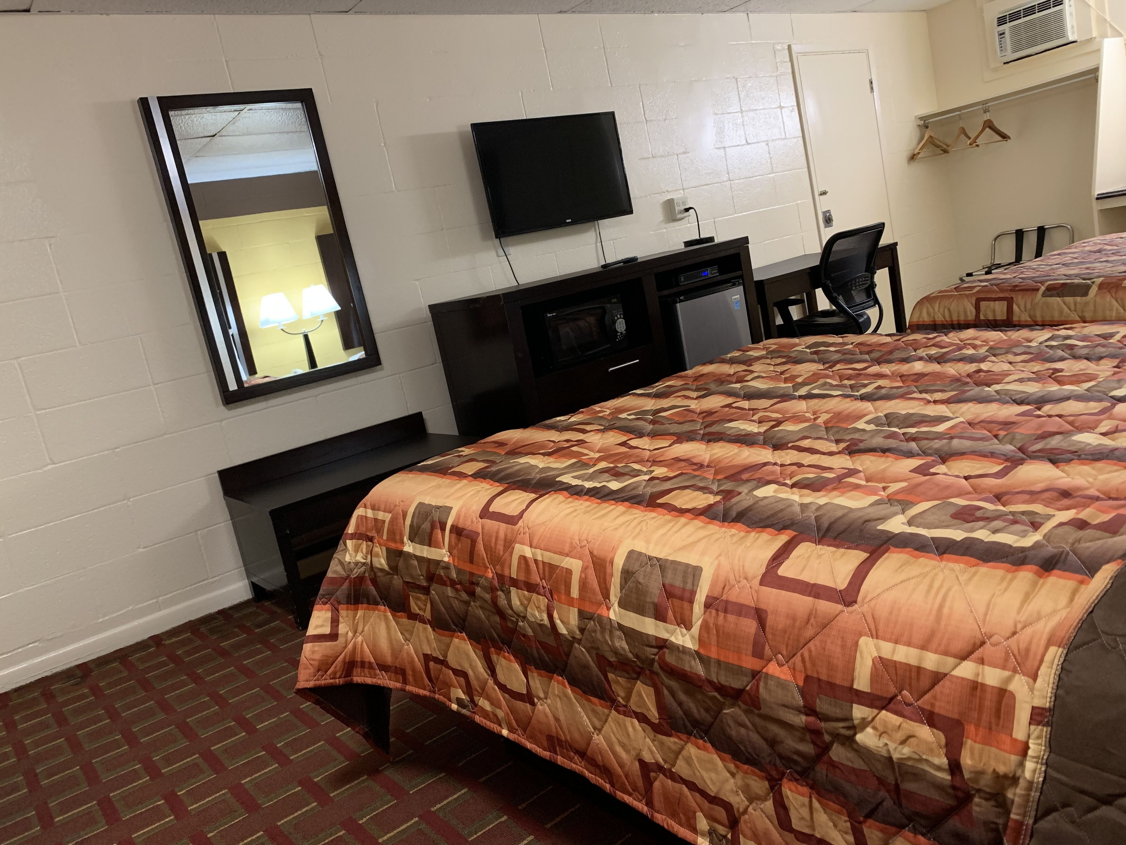 Habitación de hotel con cama, escritorio, silla, televisor y espejo.