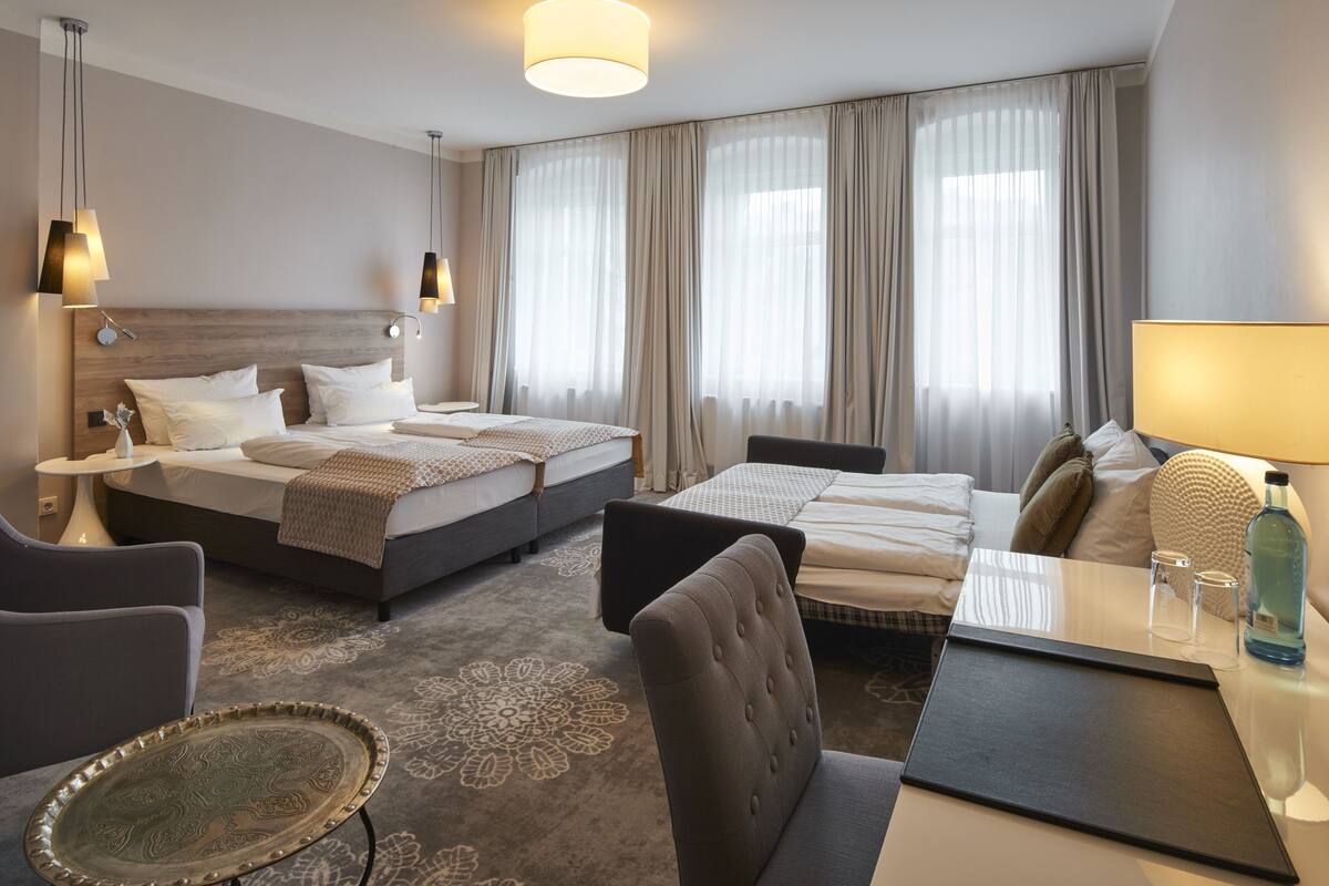 A hotel room with two beds, a sofa, a dining table, and a decorative tray.