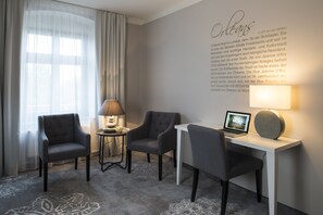 Una habitación de hotel moderna con un escritorio, dos sillones, una lámpara y una computadora portátil.