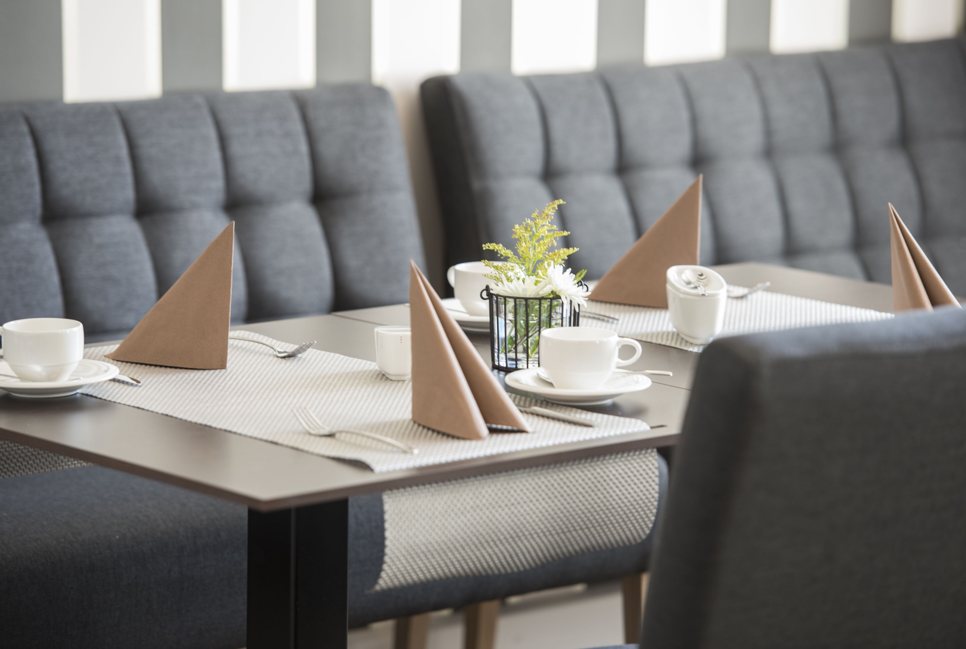 Un comedor con una mesa lista para cuatro personas, incluyendo tazas, platillos y servilletas dobladas.