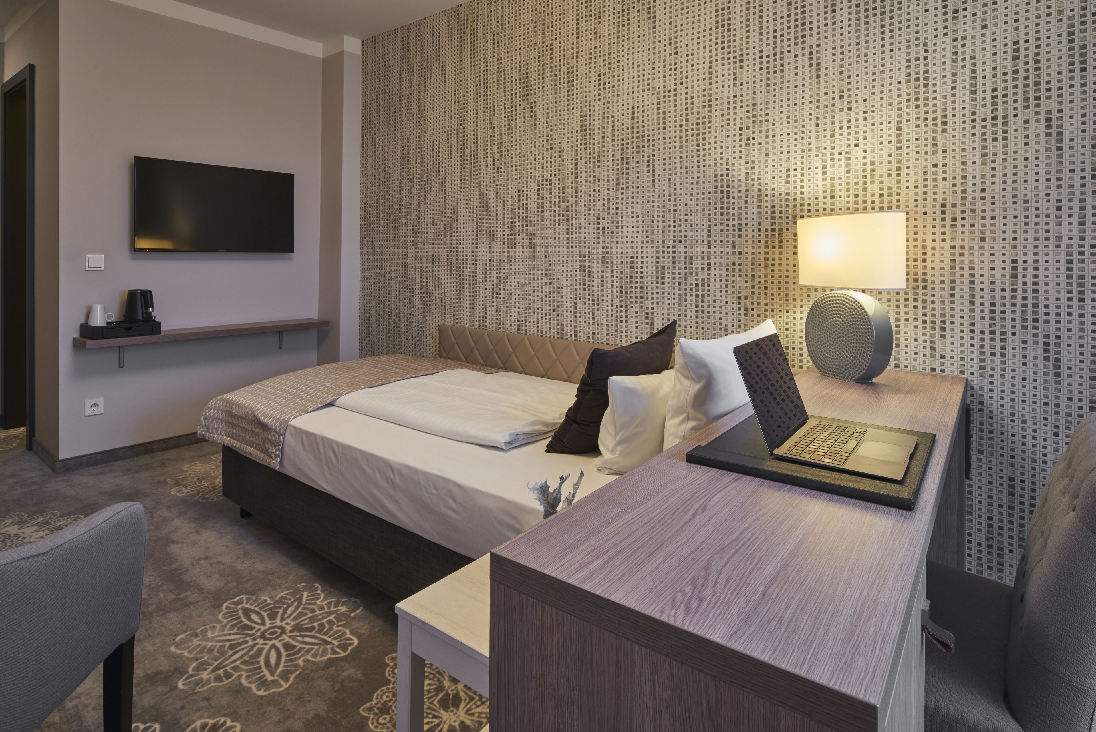 Habitación de hotel con cama, mesita de noche con una computadora portátil, televisión y lámpara de pared.