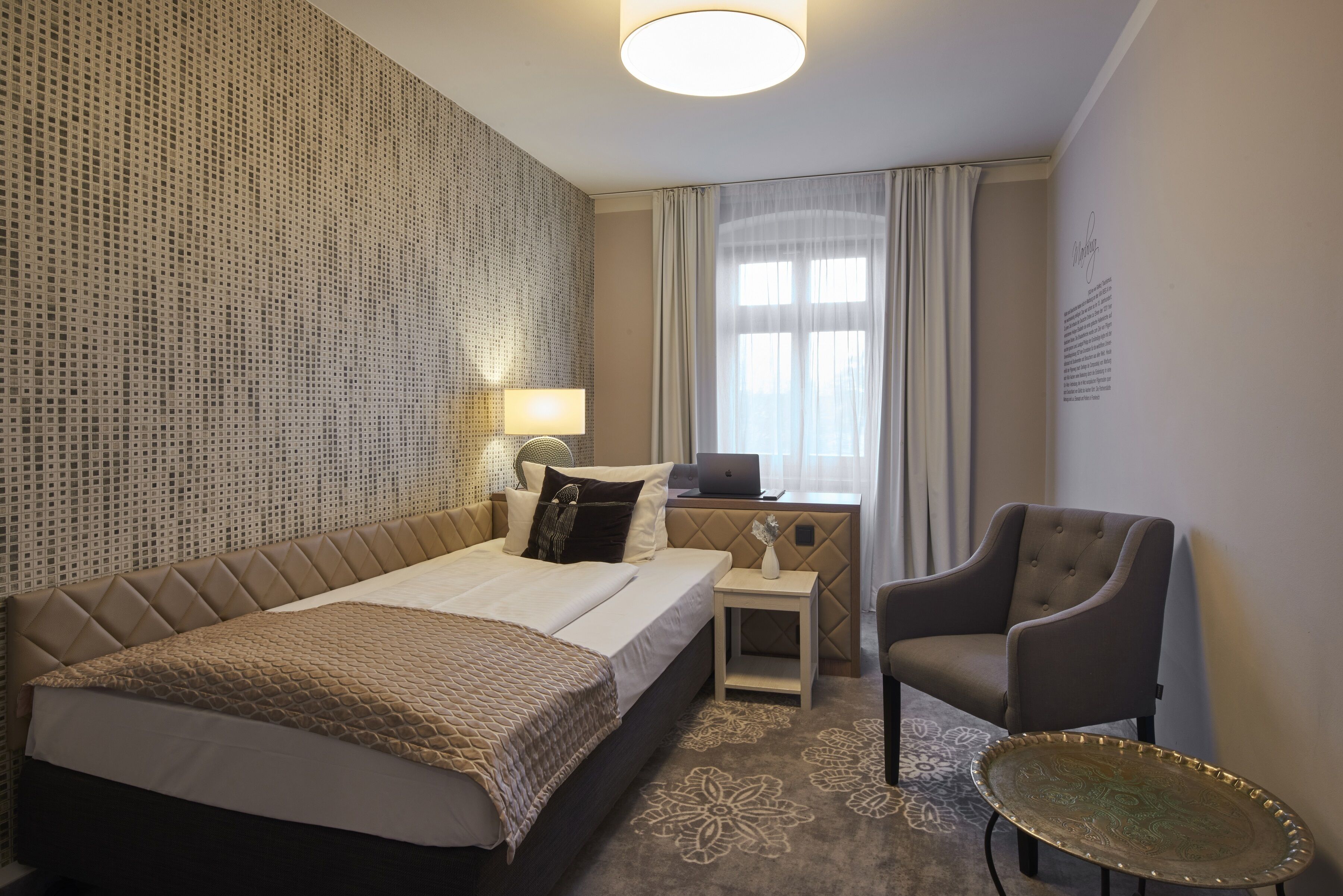 A hotel room with a bed, a chair, a desk, and a lamp.