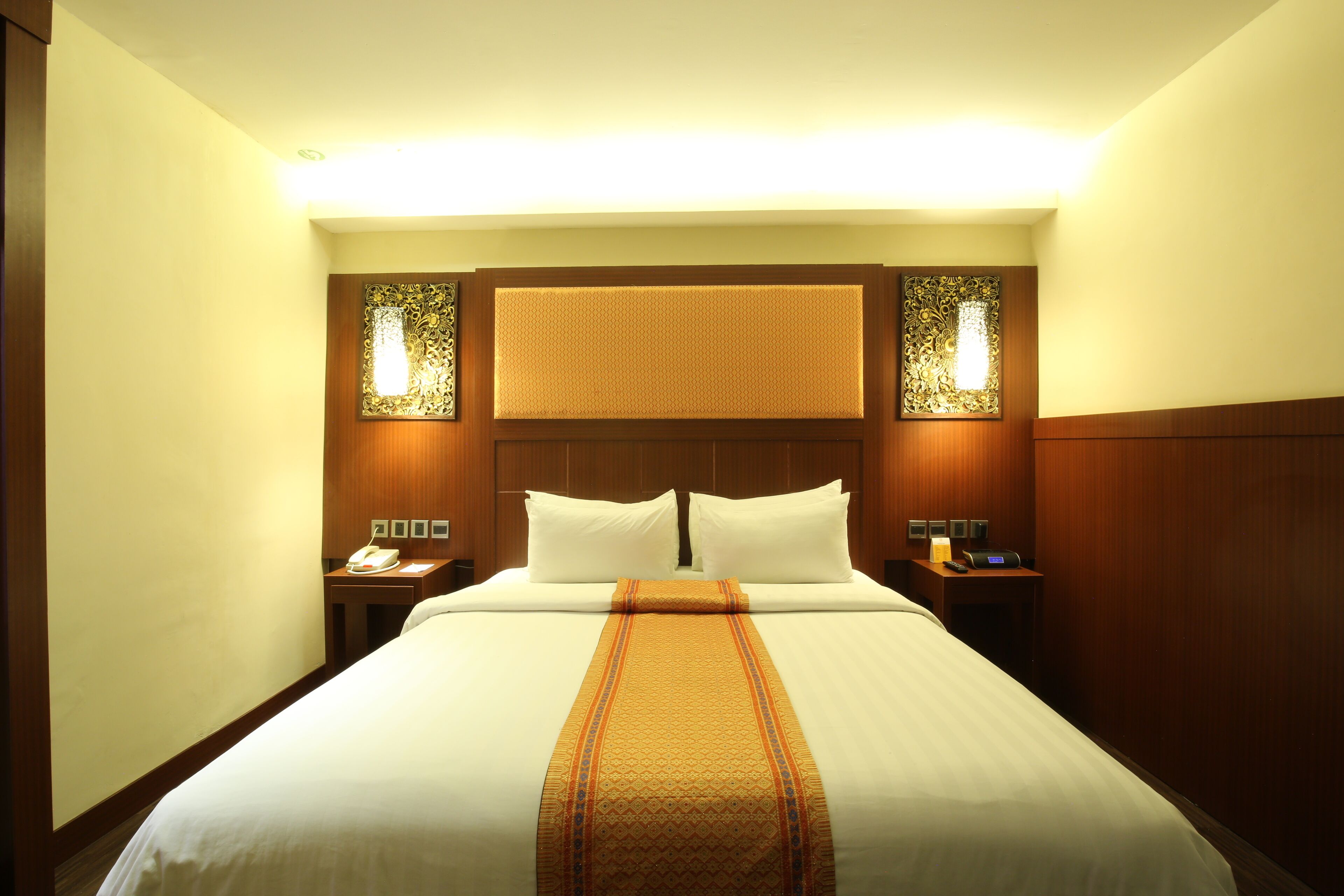 A hotel room with a large bed, two bedside tables, a telephone, and wall sconces.