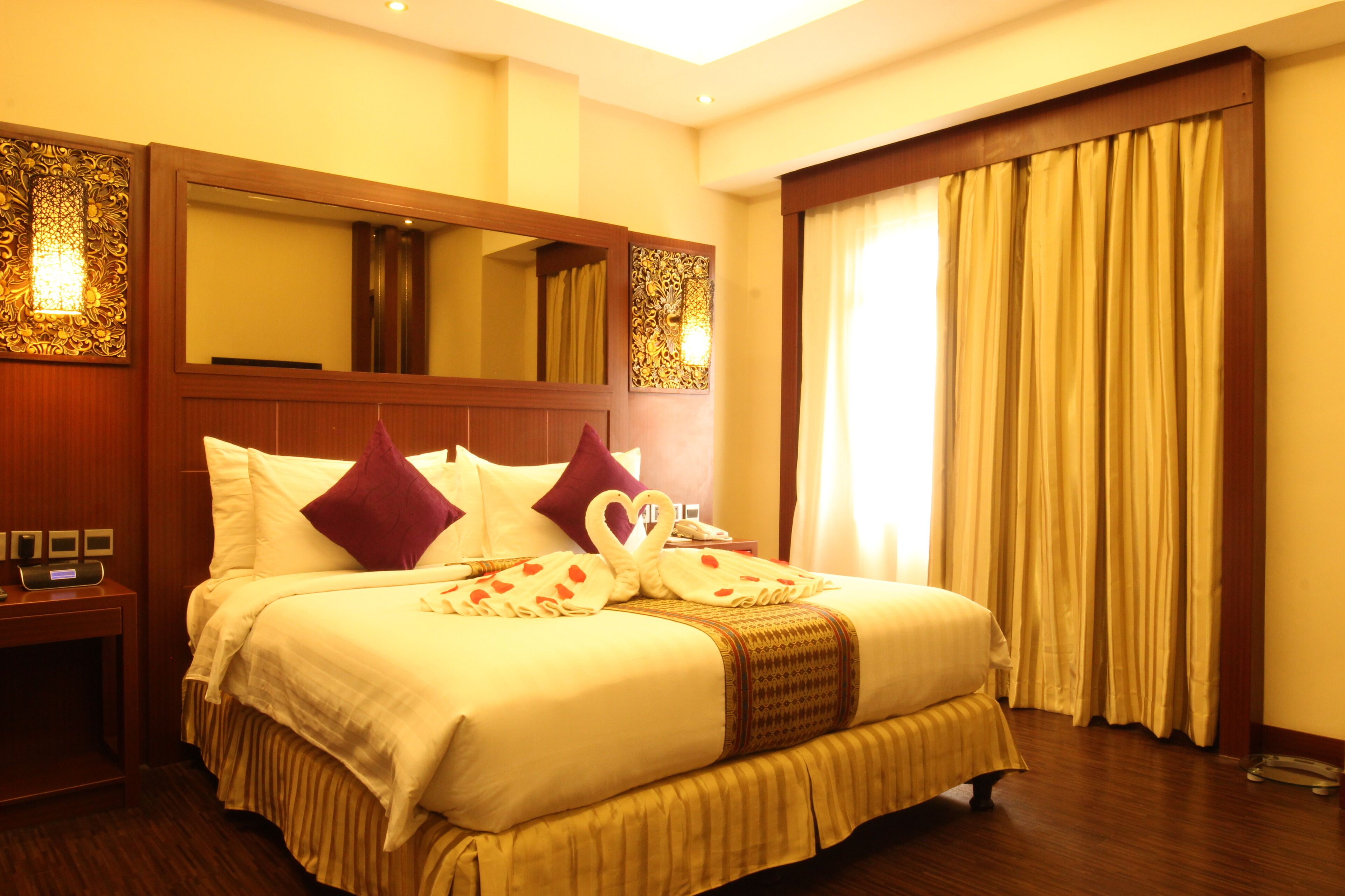 A hotel room with a large bed, a wooden headboard, a nightstand, and a mirror.