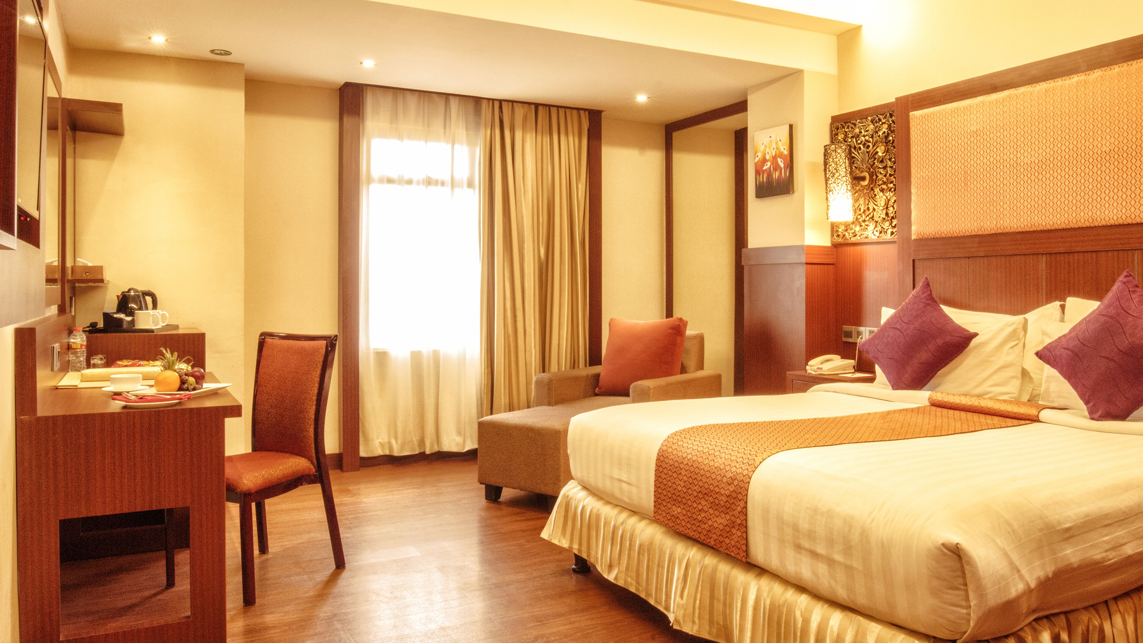 A hotel room with a bed, a desk, a chair, a nightstand, and a window with curtains.
