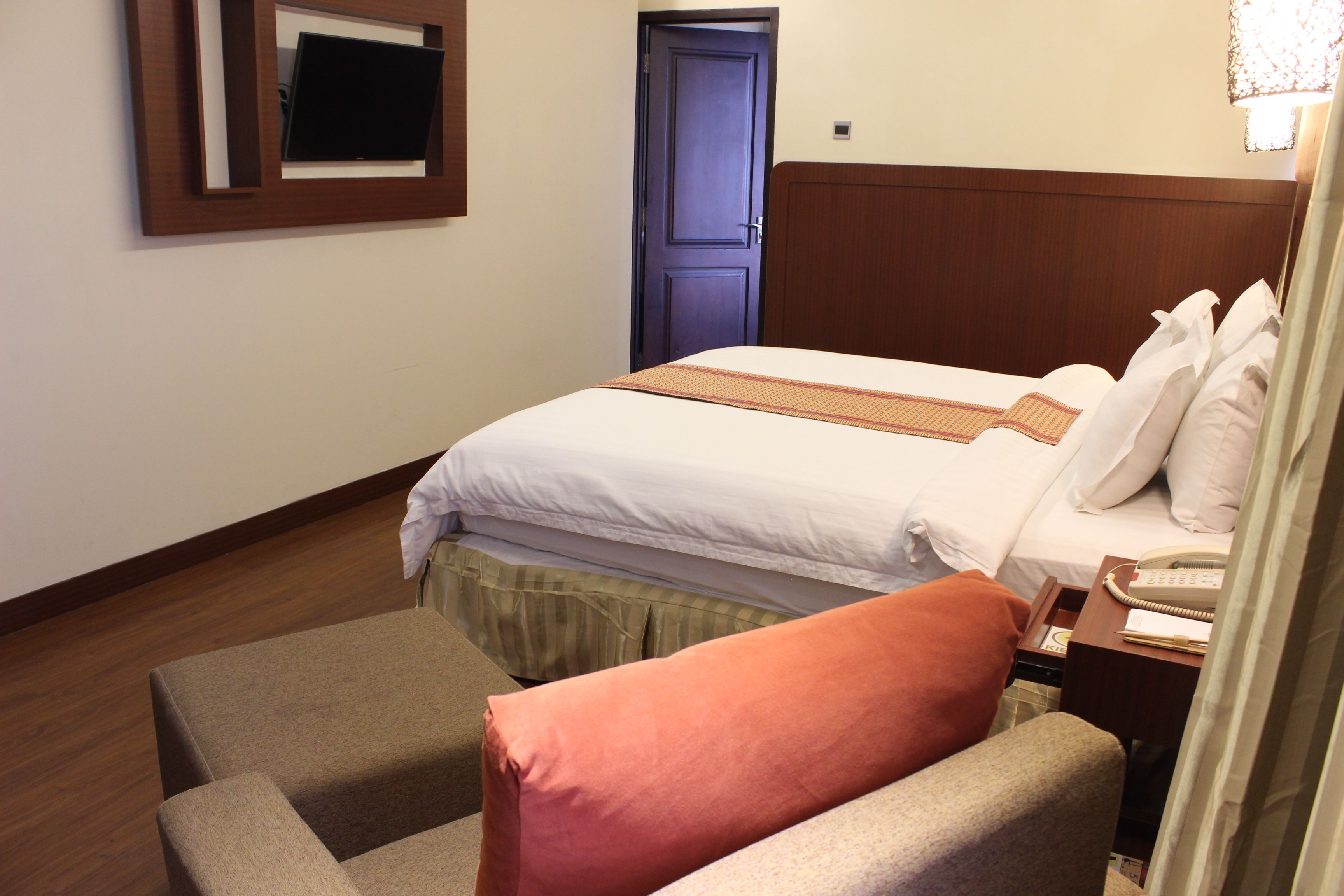 Una habitación de hotel con una cama, una silla, un escritorio con un teléfono y una puerta.