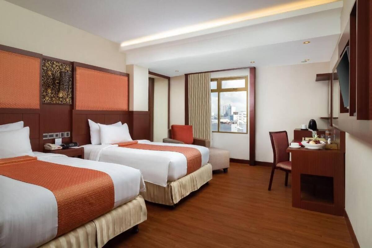 Ein Hotelzimmer mit zwei Betten, einem Schreibtisch, einem Stuhl und einem großen Fenster mit Blick auf die Stadt.