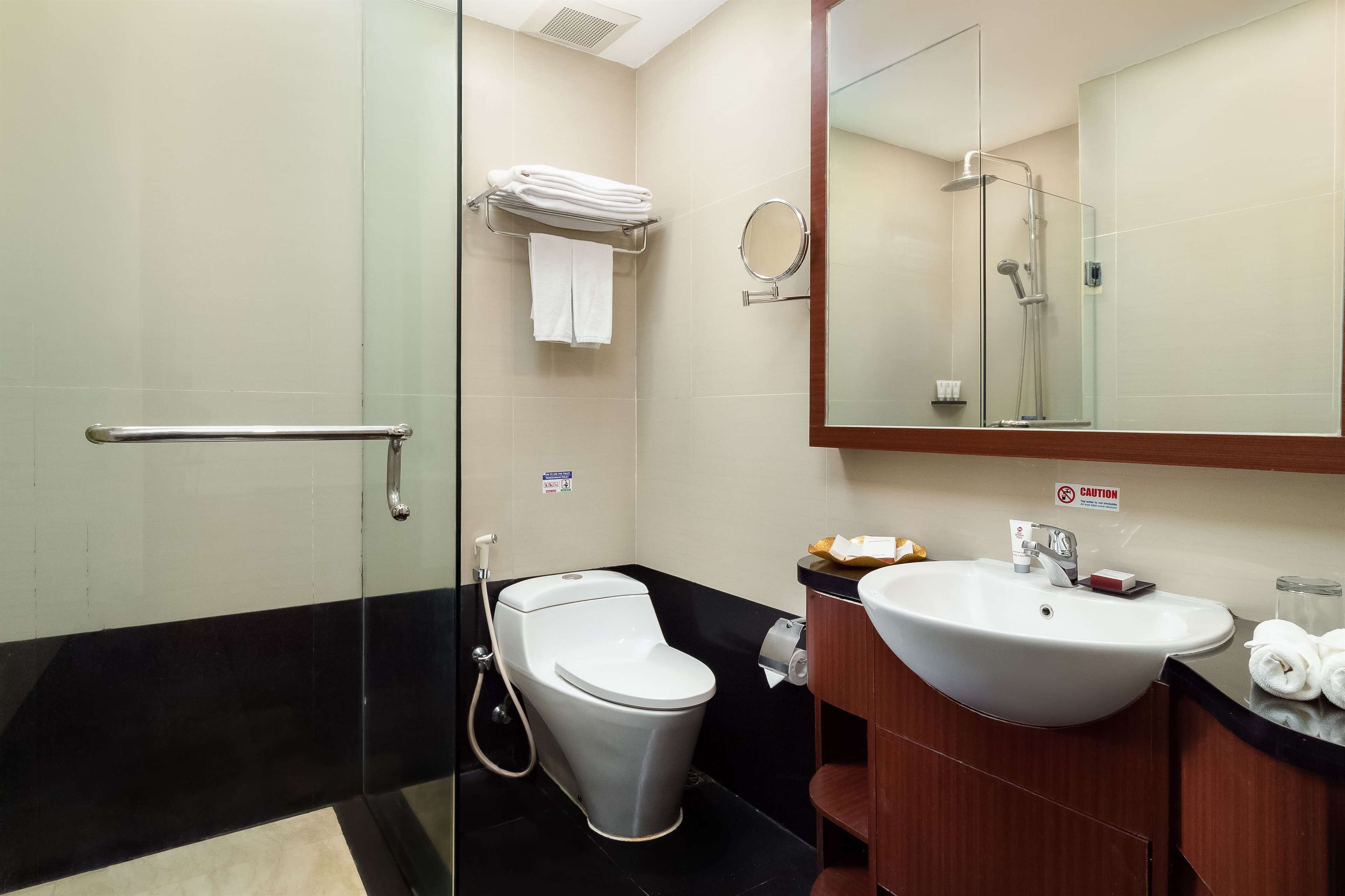 Een moderne badkamer met een douchecabine van glas, een wit toilet, een wastafel met spiegel en een handdoekhouder.