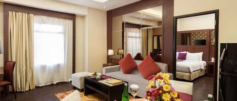 A hotel room with a sofa, a dining table with a vase of flowers, a bed, and a large mirror.