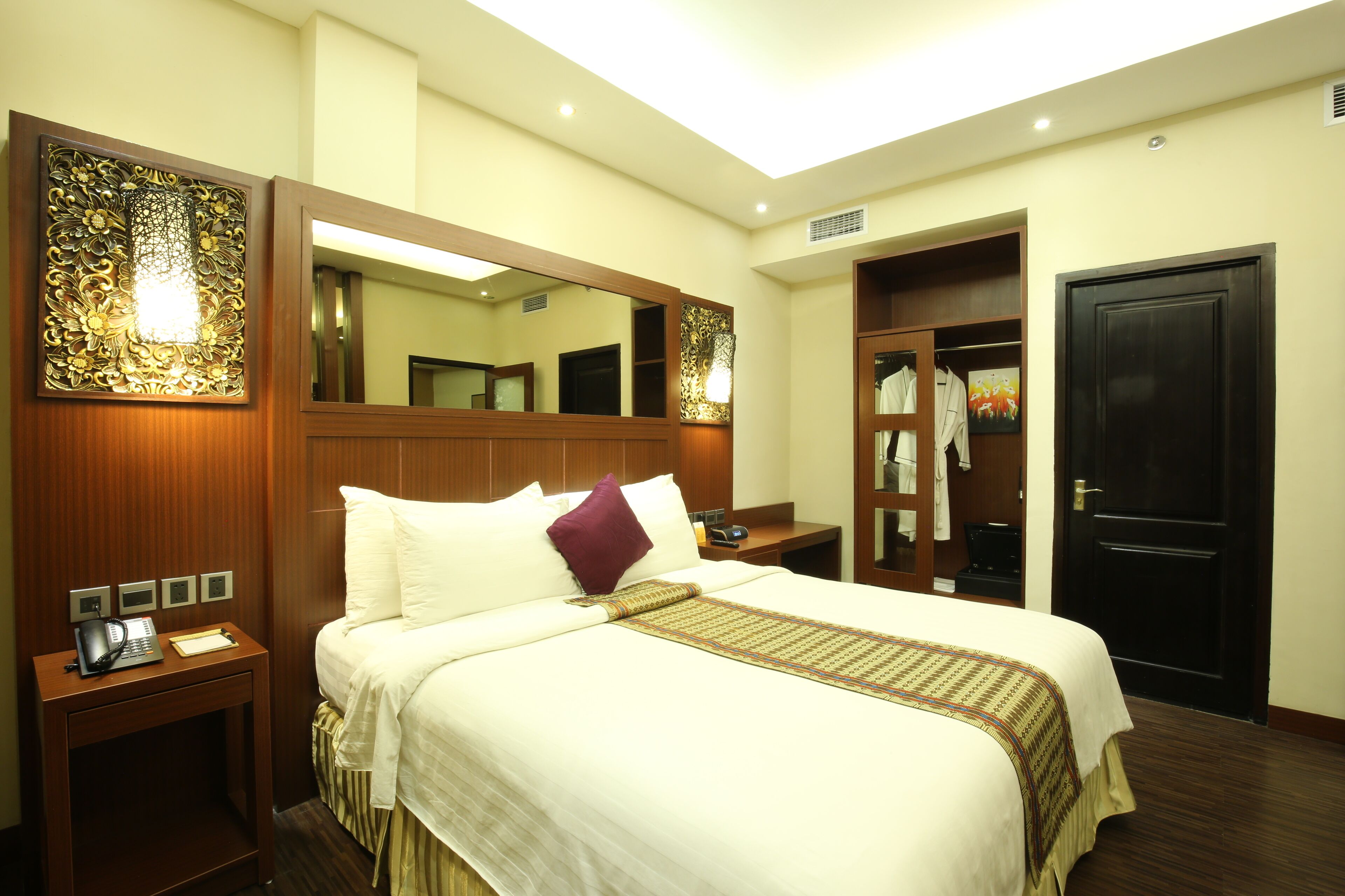 A hotel room with a large bed, a bedside table with a phone, a mirror, and a wardrobe.