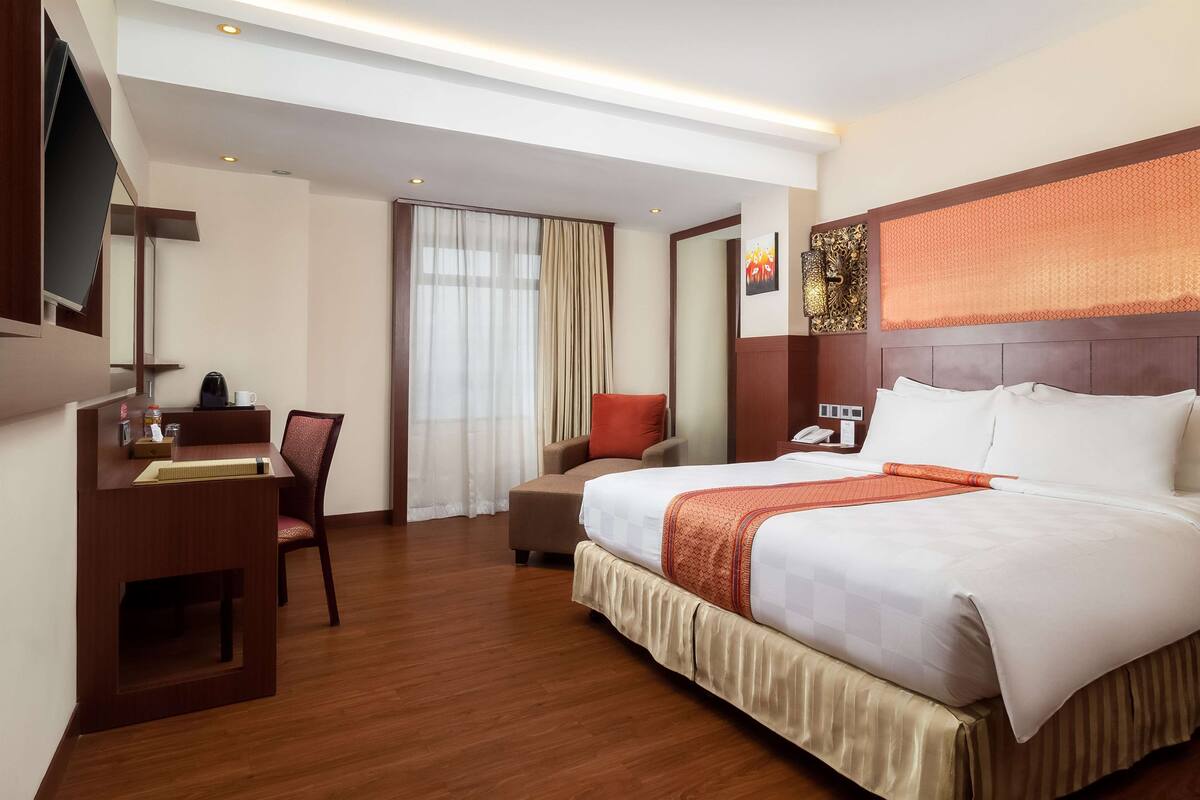 Ein Hotelzimmer mit einem großen Bett, einem Schreibtisch mit Stuhl, einem Fernseher und einem Fenster mit Vorhängen.