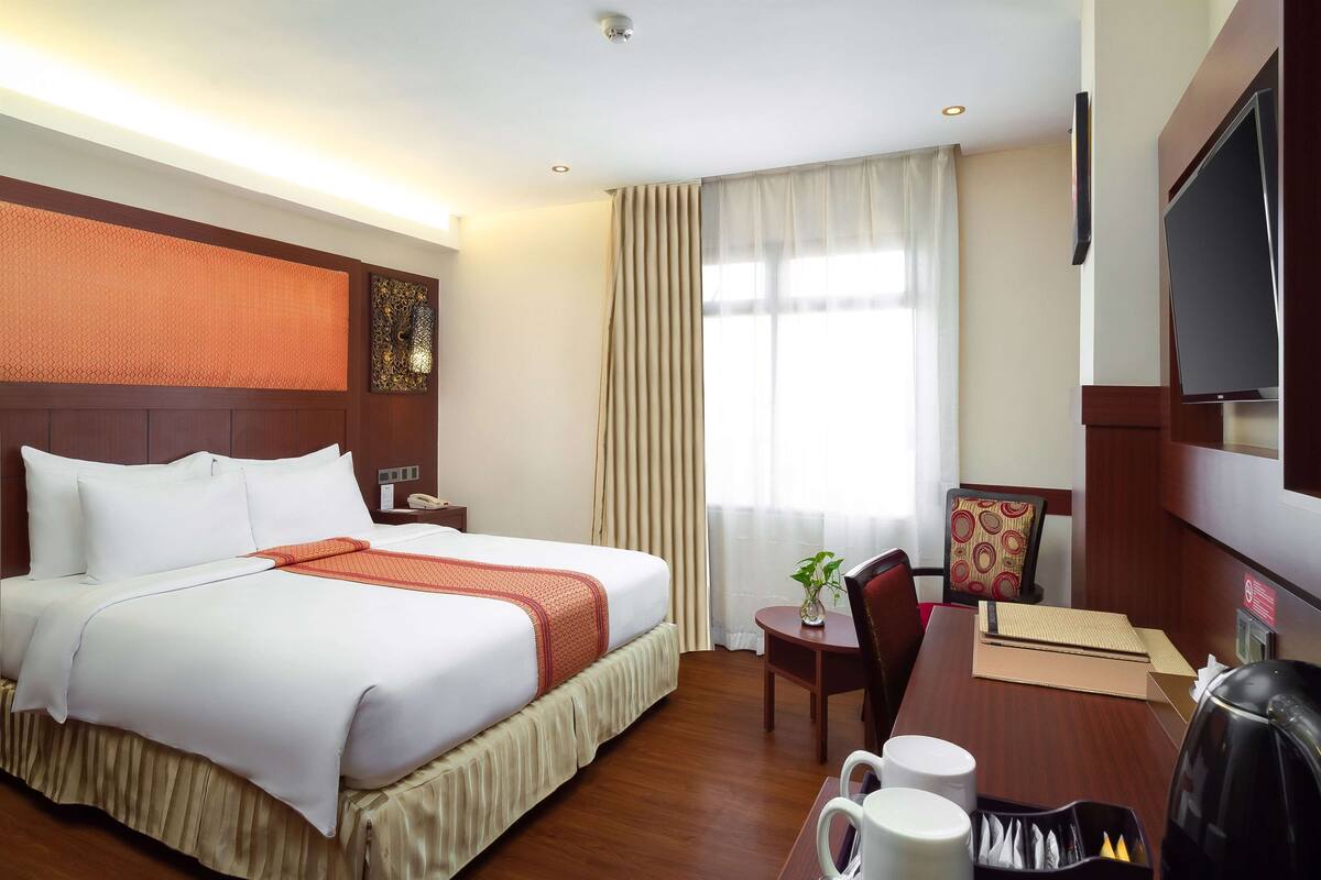 Ein Hotelzimmer mit einem großen Bett, einem Schreibtisch mit Stuhl, einem Fernseher und einer Kaffeemaschine.