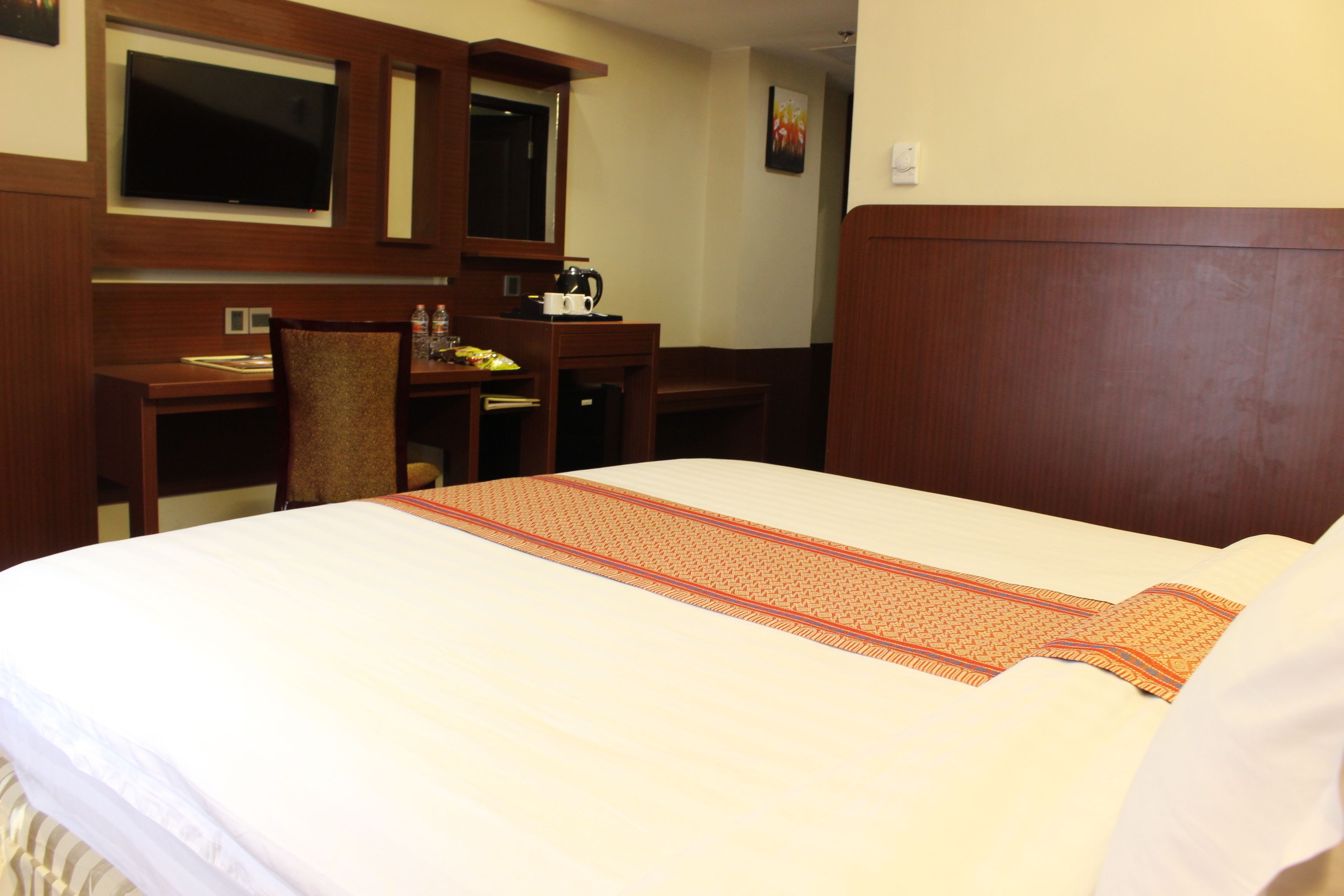 A hotel room with a large bed, a desk, a chair, a television, and a coffee maker.
